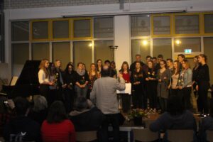 Schülerchor bei einem Auftritt vor Publikum in einem Saal.
