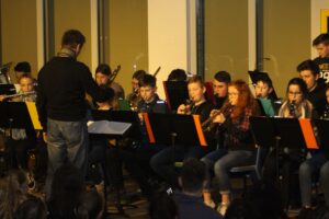 Schüler spielen bei einem Konzert im Ensemble. Ein Dirigent leitet die Aufführung.