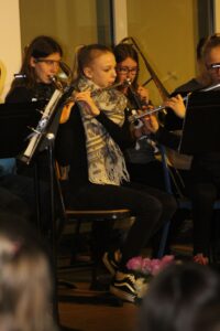 Schülerin spielt Flöte in einem Blasorchester. Blumen im Vordergrund sichtbar.