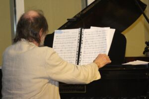 Ein Musiker spielt am Klavier und schaut auf Notenblätter.