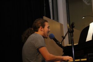 Musiker spielt am Klavier und singt in ein Mikrofon.