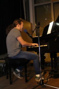 Ein junger Mann spielt am Klavier und singt in ein Mikrofon.