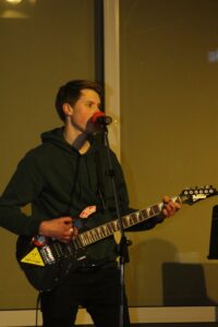 Junger Mann spielt E-Gitarre und singt in ein Mikrofon.