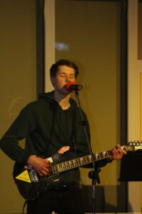 Ein junger Mann singt und spielt Gitarre während einer Aufführung.