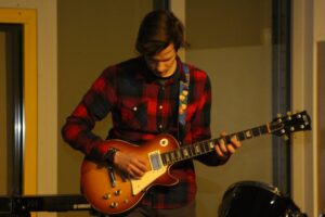 Ein junger Mann spielt E-Gitarre auf einer Bühne.