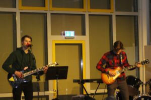 Zwei Musiker spielen live auf einer Bühne. Ein Gitarrist singt, der andere spielt E-Gitarre.