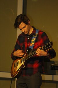 Junger Mann spielt E-Gitarre auf einer Bühne.
