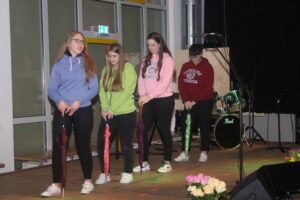 Vier Schülerinnen in bunten Sweatshirts führen eine Tanzperformance auf.