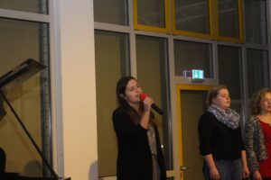 Eine Frau singt mit Mikrofon, zwei weitere Personen stehen daneben.