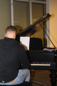 Junger Mann sitzt an einem Klavier und spielt. Blatt Musik liegt darauf.