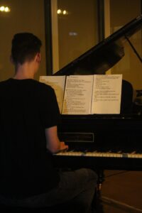 Junger Mann spielt Klavier mit Noten vor sich.