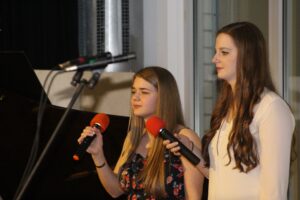 Zwei Mädchen singen mit Mikrofonen auf einer Bühne.