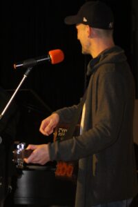 Ein Mann mit einer Gitarre steht am Mikrofon und schaut zur Seite.