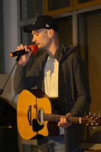 Mann mit Gitarre singt ins Mikrofon auf einer Bühne.