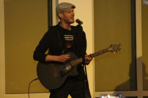 Mann spielt Gitarre und singt vor einem Mikrofon auf der Bühne.