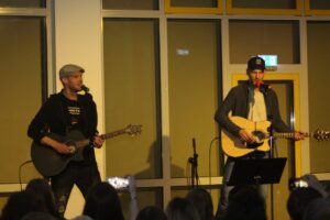 Zwei Musiker mit Gitarren spielen auf einer Bühne vor Publikum.