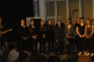 Schülerinnen und Schüler singen auf einer Bühne, begleitet von einem Gitarristen.