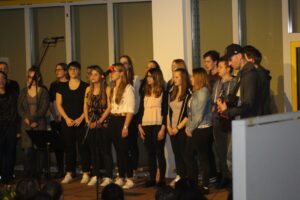 Schüler stehen in Reihe auf der Bühne und singen gemeinsam.