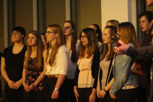 Schülerinnen und Schüler singen auf einer Bühne in einem Chor.