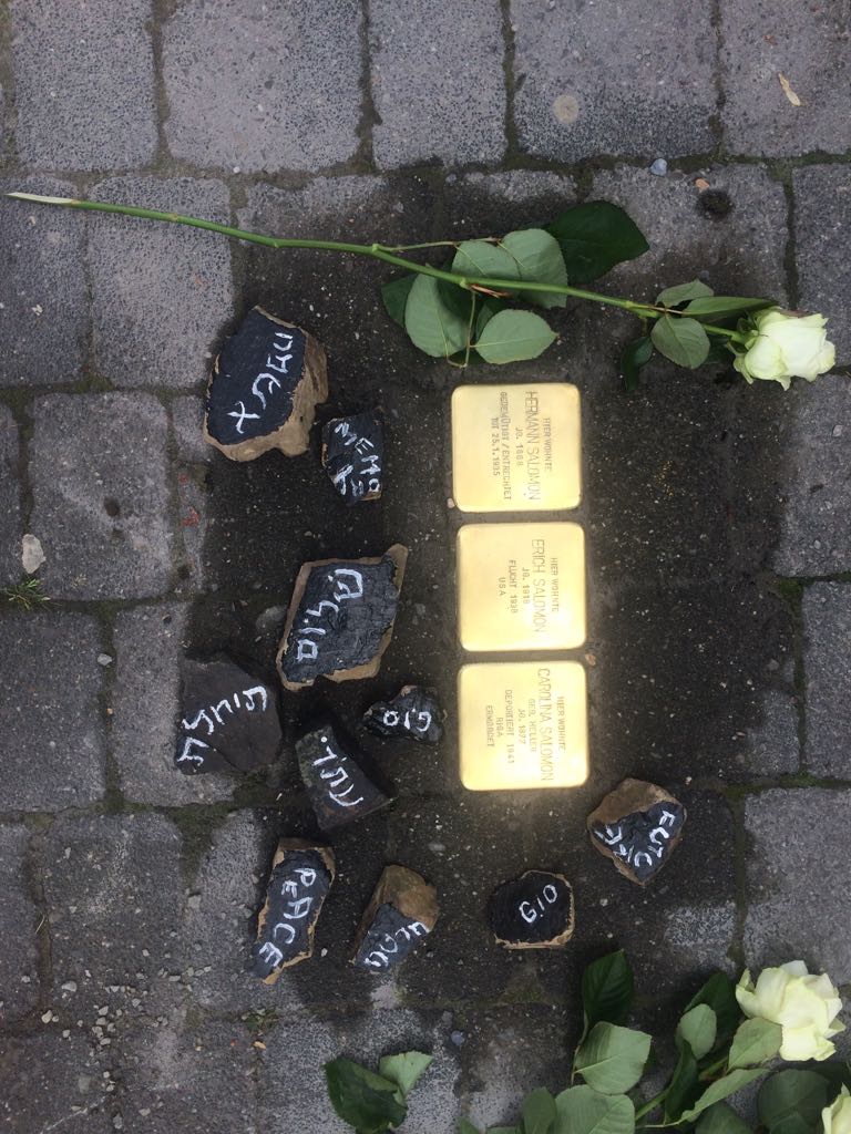Stolpersteine mit Gedenksteinen und weißen Rosen auf einem Pflasterweg.