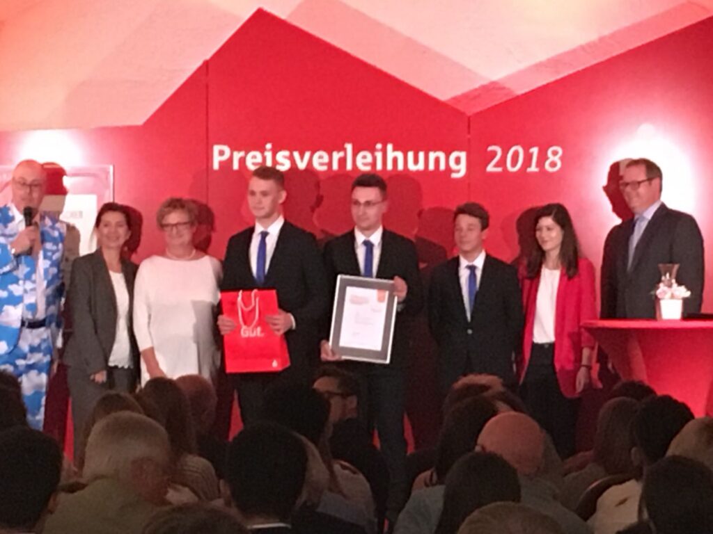 Preisverleihung 2018 mit mehreren Personen auf der Bühne und Auszeichnung.