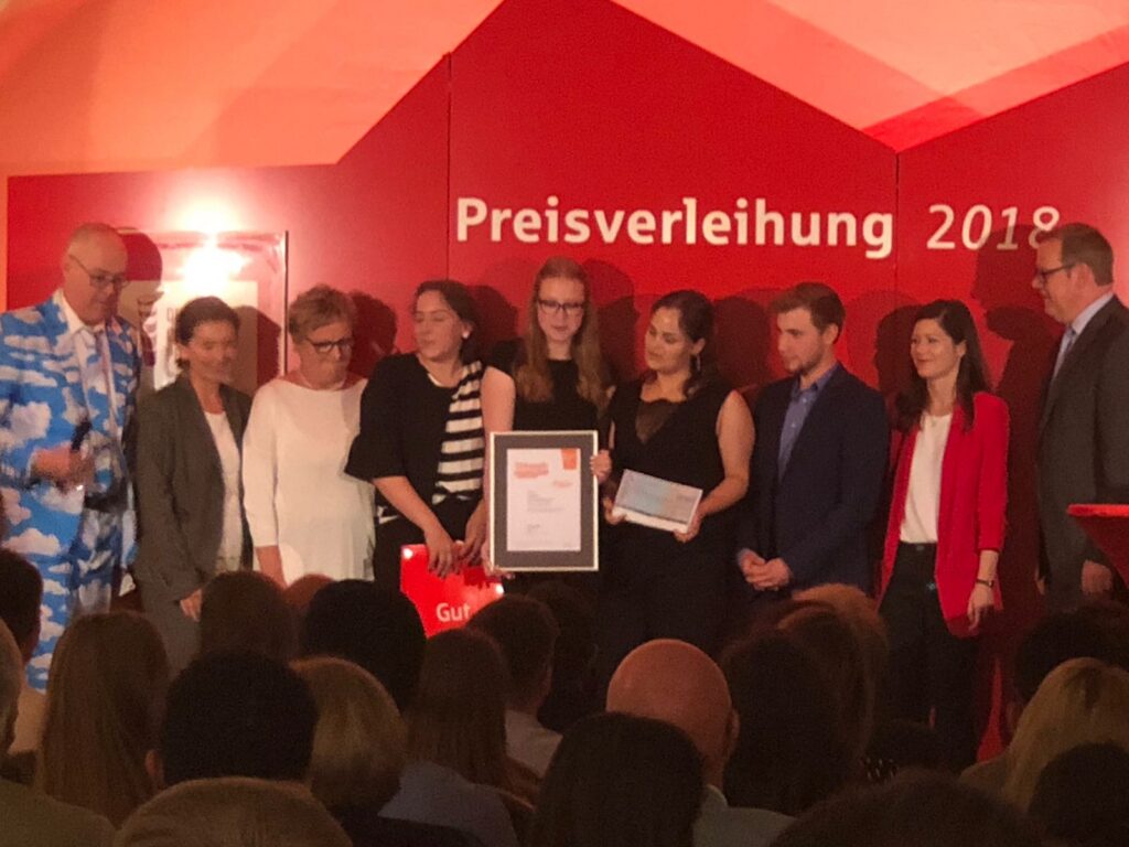 Preisverleihung 2018 mit mehreren Personen auf der Bühne und Urkundenübergabe.