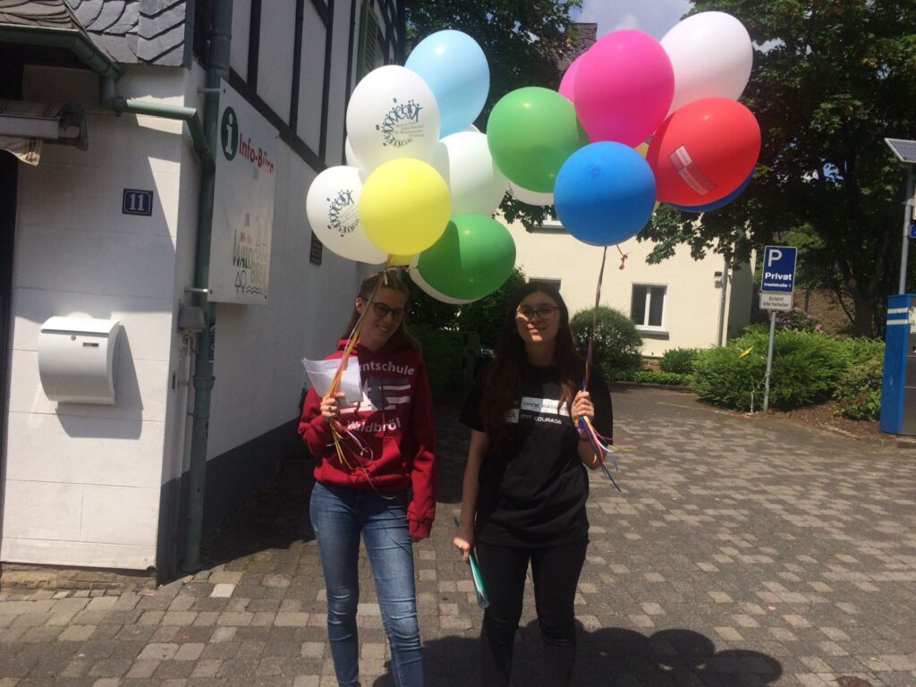 Zwei Mädchen gehen mit bunten Luftballons auf der Straße.