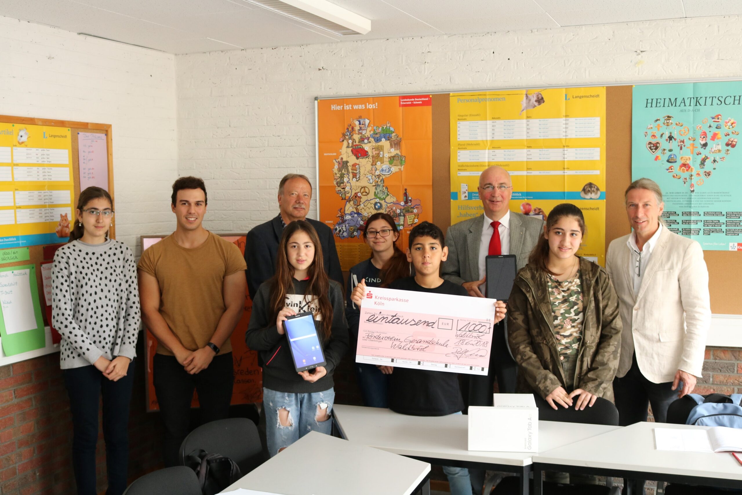Gruppe von Schülern und Lehrern in einem Klassenzimmer mit Tablets und einem Scheck.