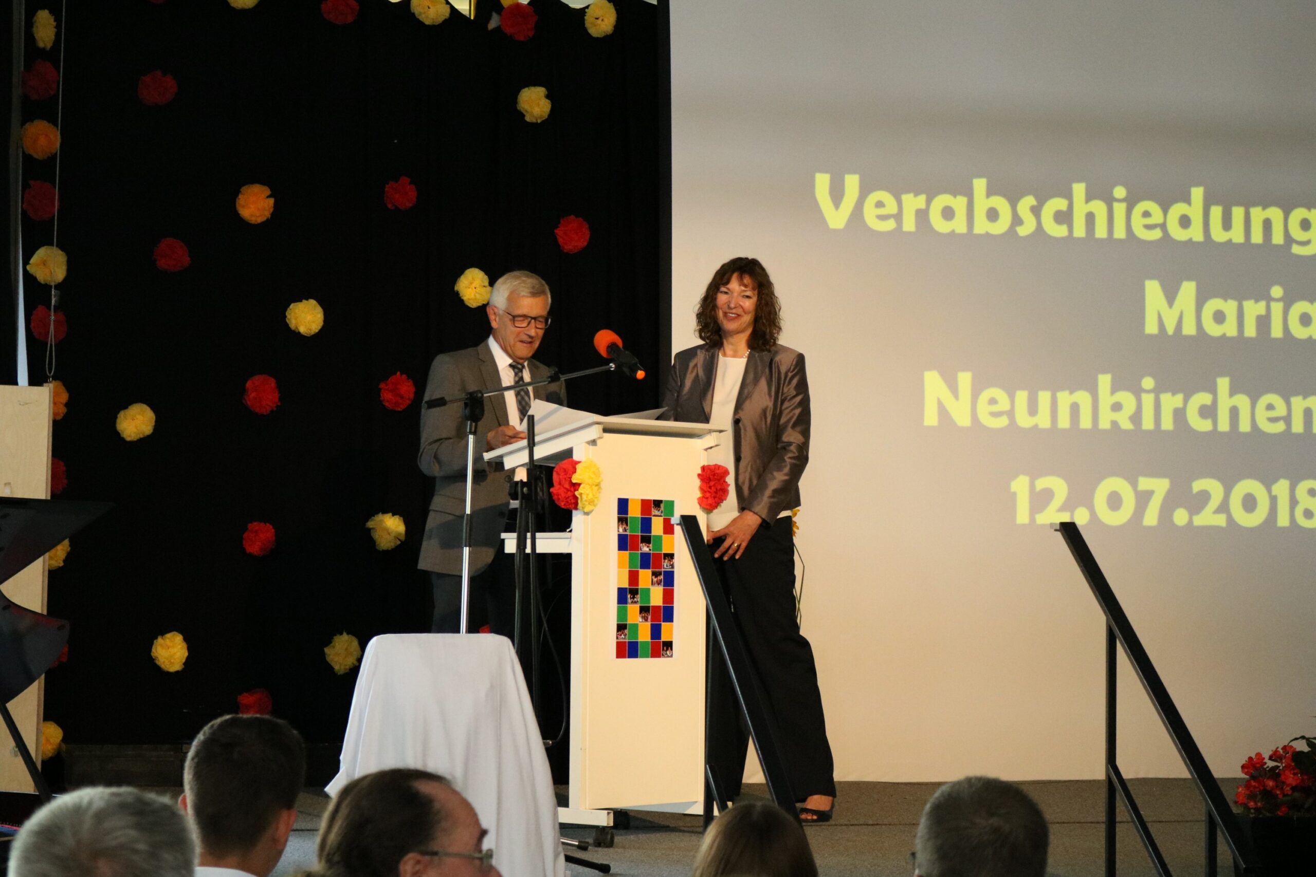 Zwei Personen stehen am Rednerpult bei einer Verabschiedungsfeier.