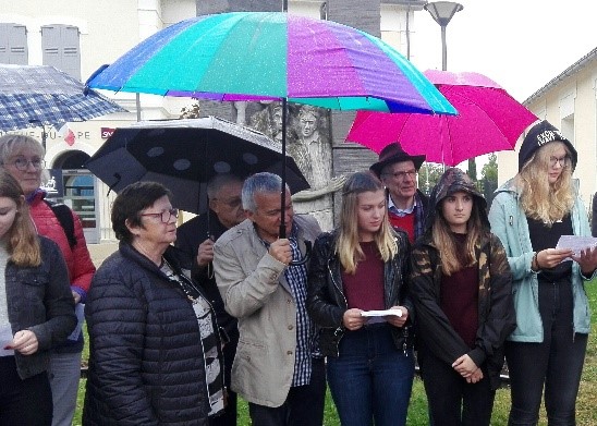 Menschen stehen unter Regenschirmen und lesen Dokumente vor einem Denkmal.