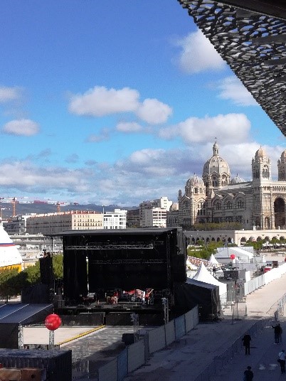 Blick auf einen Festivalbereich mit Bühne und Stadtansicht im Hintergrund.