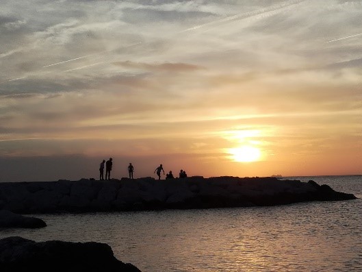 Silhouetten von Menschen auf einem Steg bei Sonnenuntergang über dem Wasser.