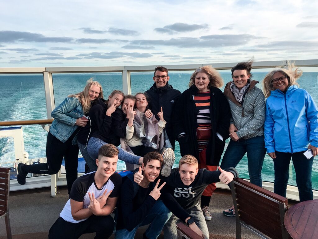 Gruppe von Jugendlichen und Erwachsenen auf einem Schiff, lächelnd und posierend.