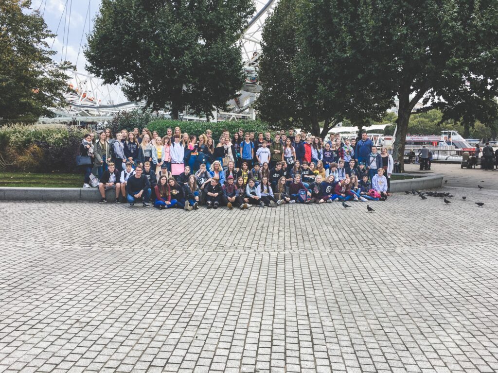 Gruppenfoto von Schülern und Lehrern im Freien, umgeben von Bäumen und einer Parklandschaft.