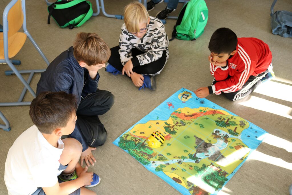 Vier Kinder sitzen im Kreis um einen bunten Spielteppich.