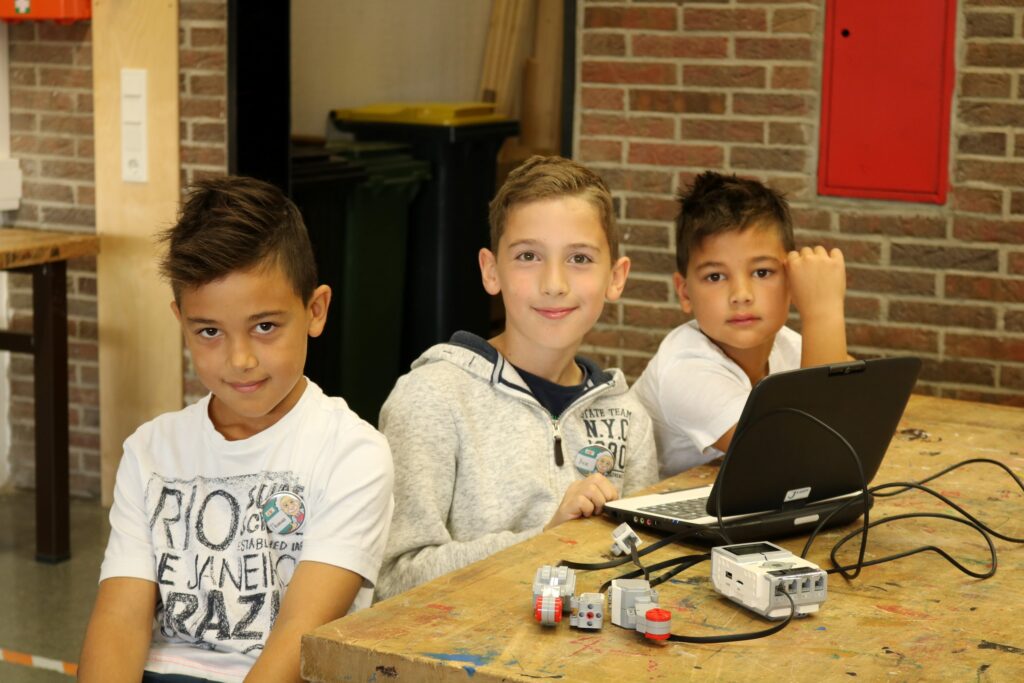 Drei Jungen sitzen an einem Tisch und arbeiten an einem Laptop.