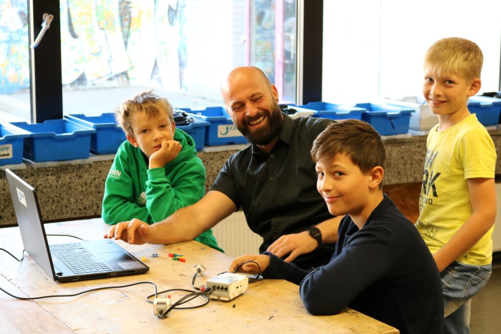 Lehrer zeigt Kindern etwas am Laptop, sie lachen und arbeiten zusammen.