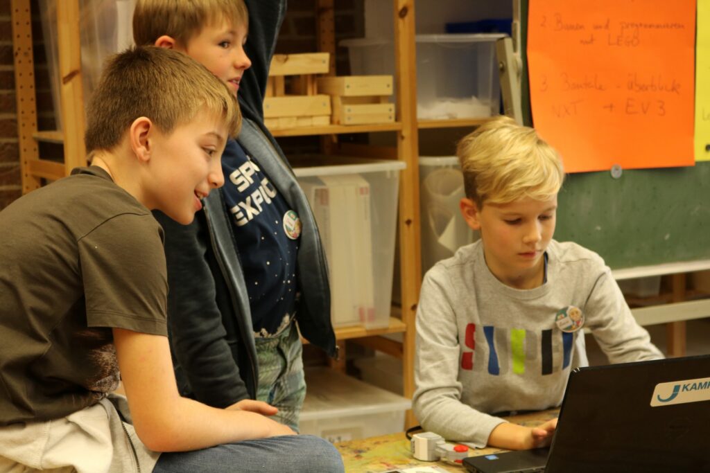 Drei Kinder sitzen zusammen und schauen auf einen Laptop.