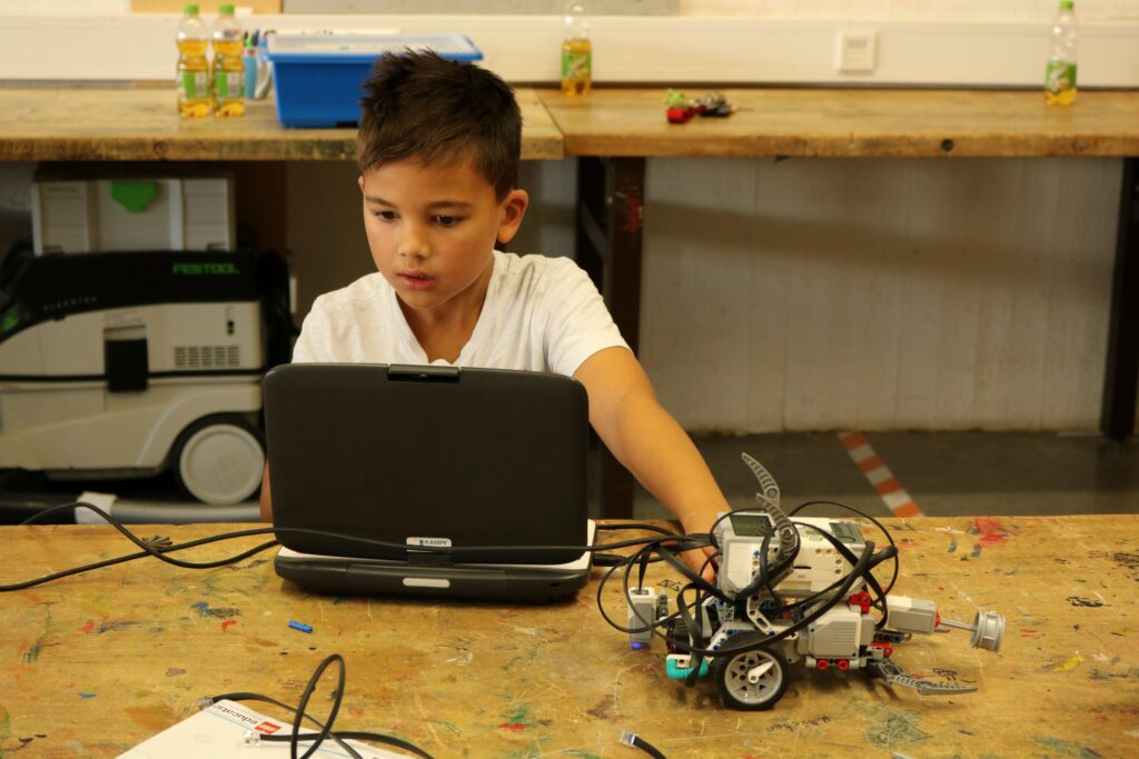 Ein Junge sitzt an einem Tisch und arbeitet an einem Roboter mit Laptop.