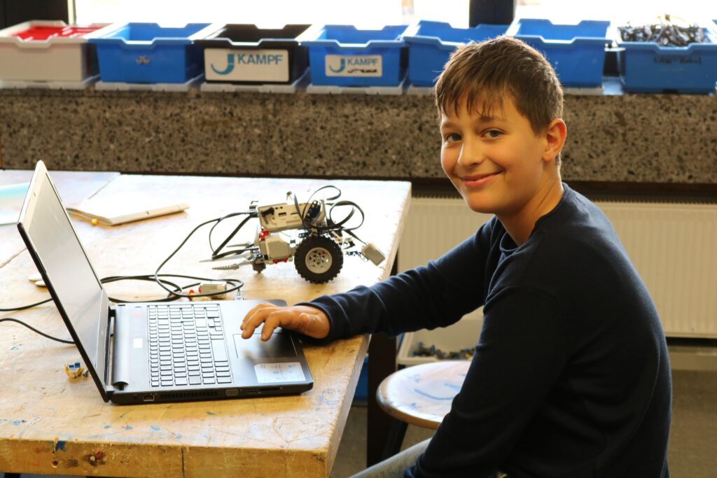 Ein Junge sitzt an einem Laptop und arbeitet an einem Robotermodell.
