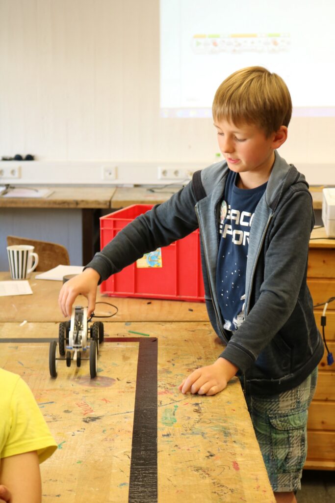 Schüler testet ein selbstgebautes Fahrzeug auf Tisch in einem Klassenraum.