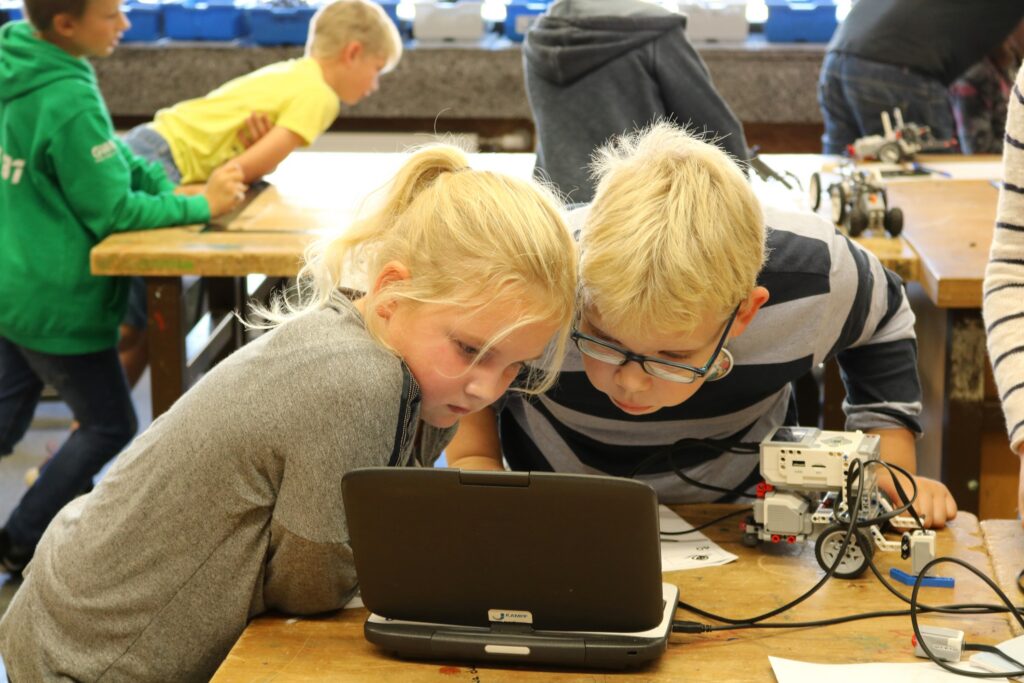 Zwei Kinder arbeiten konzentriert an einem Laptop in einem Klassenraum.