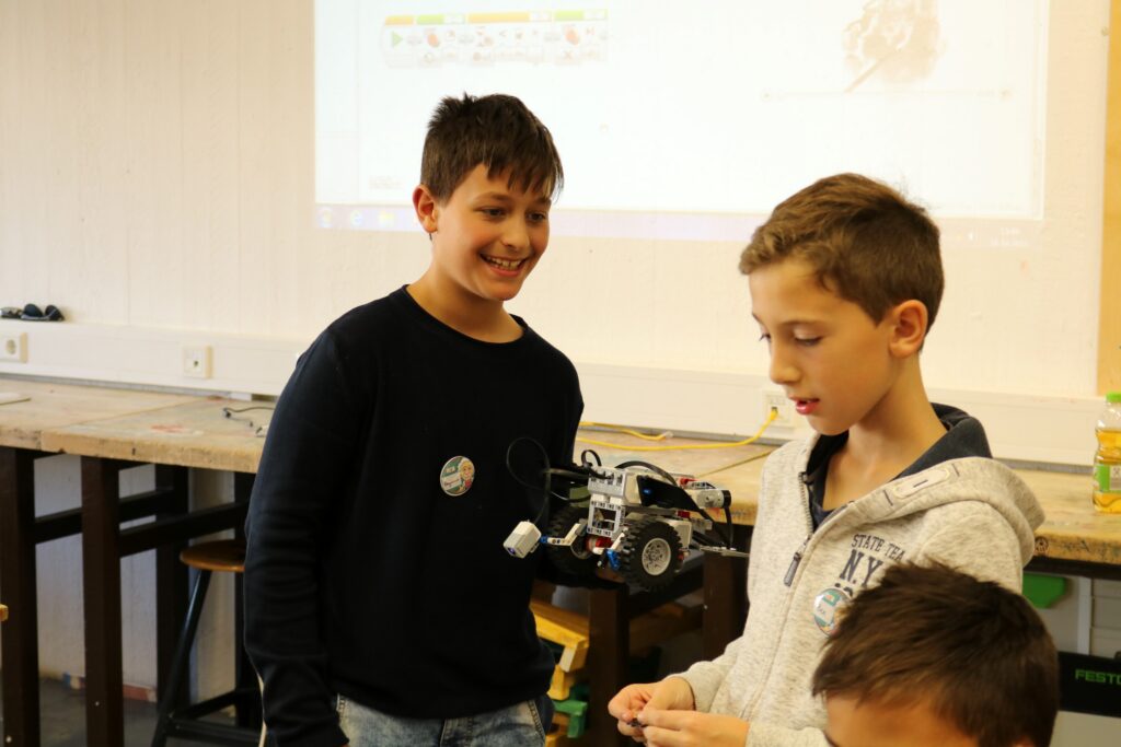 Zwei Schüler stehen am Tisch und betrachten einen Roboter.