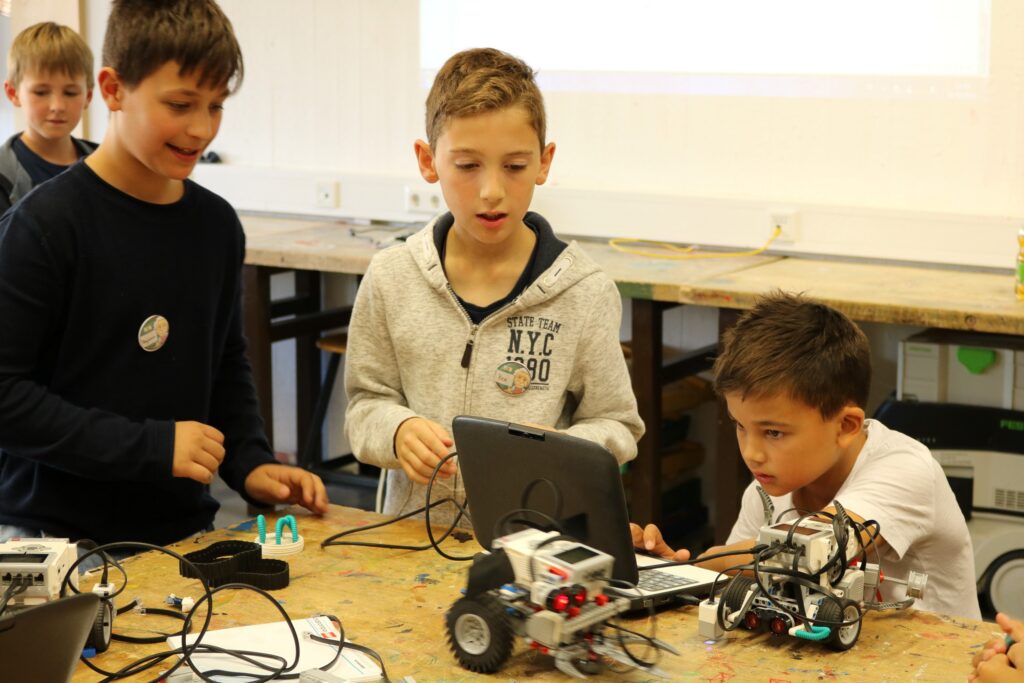 Kinder arbeiten an einem Roboterprojekt mit Tablets und Bauteilen.