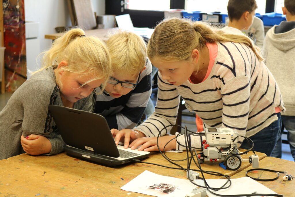 Kinder arbeiten gemeinsam an einem Laptop und einem Roboter.