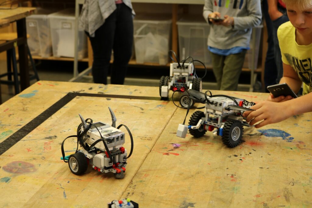 Kinder steuern Roboter auf einem Tisch in einem Schulraum.