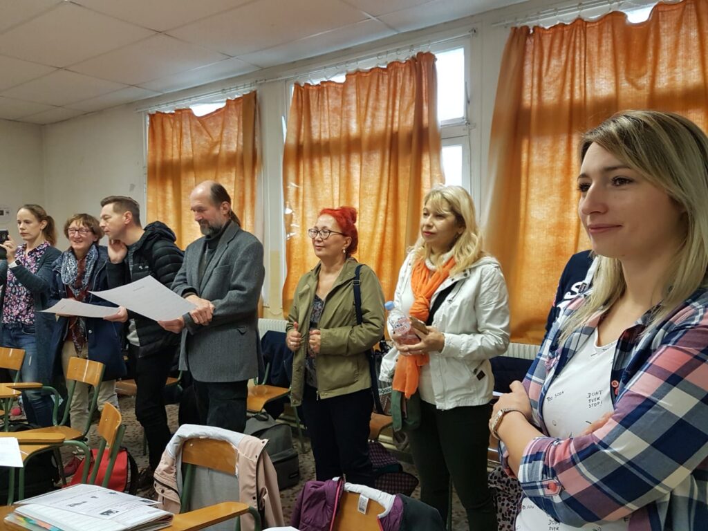 Gruppe von Erwachsenen in einem Klassenzimmer, einige halten Unterlagen in der Hand.