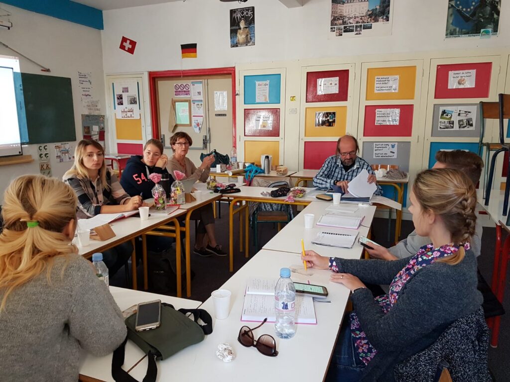 Lehrer und Schüler sitzen an Tischen in einem Klassenzimmer und arbeiten zusammen.