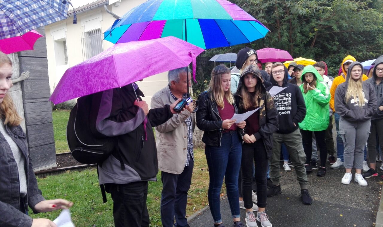 Schüler und Lehrer stehen im Freien unter Regenschirmen.