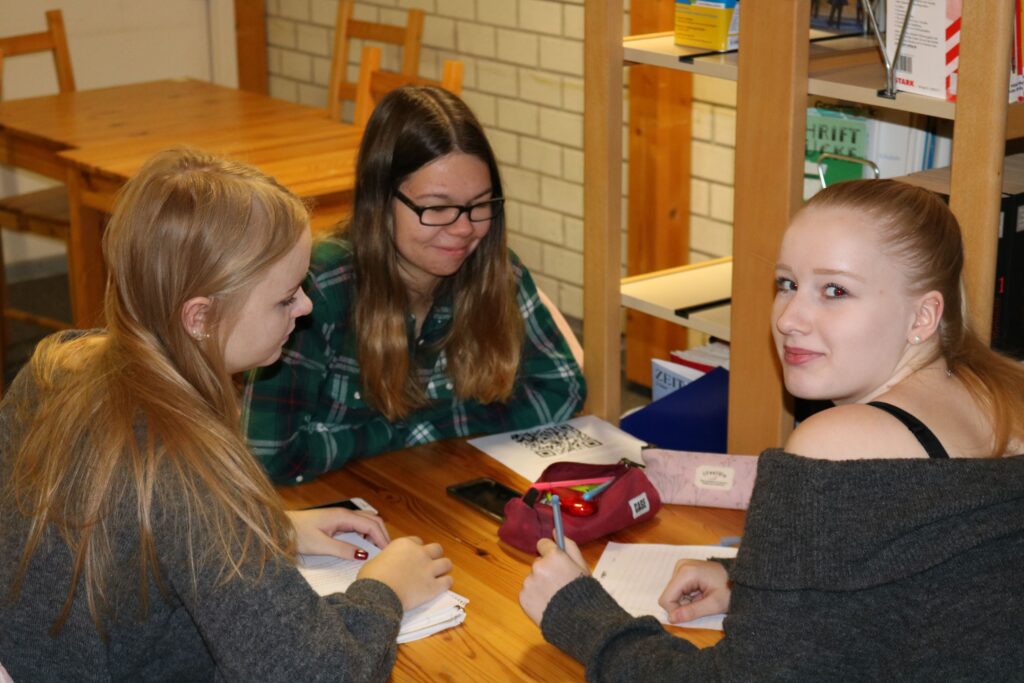 Drei Schülerinnen sitzen an einem Tisch und arbeiten gemeinsam an ihren Aufgaben.